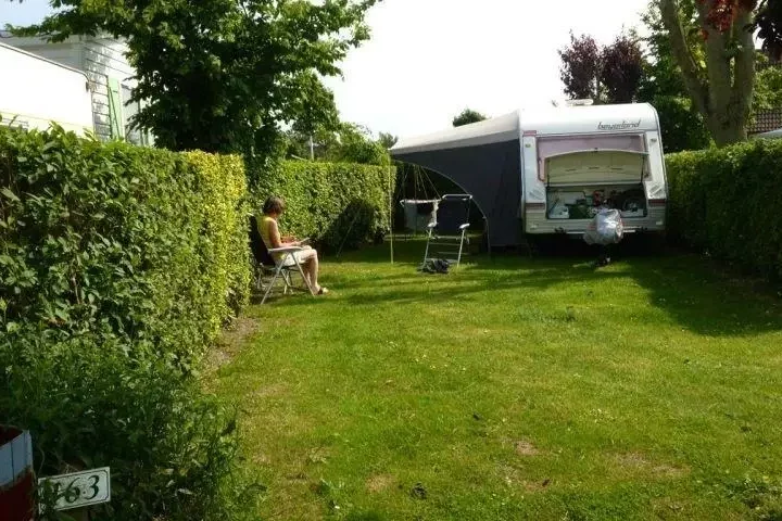 Jardin verdoyant avec une caravane et une personne assise.