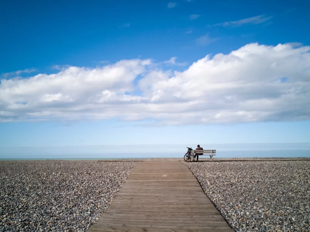 Homme assis sur un banc, vue sur la mer.