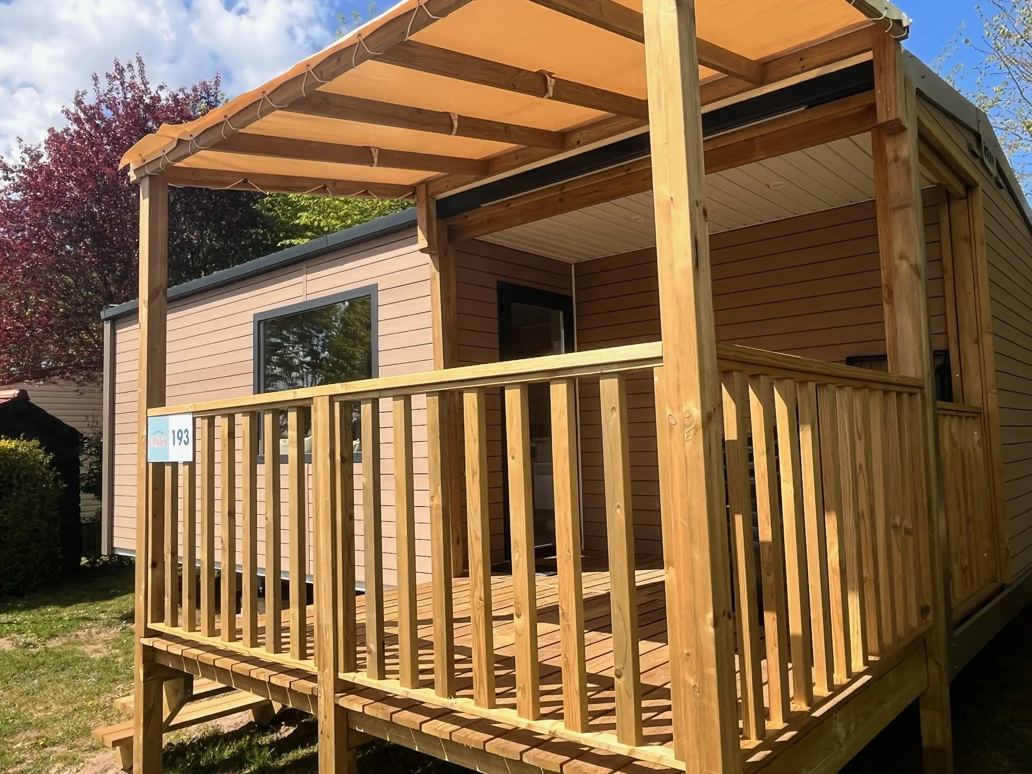 Mobil-home avec terrasse en bois et auvent.