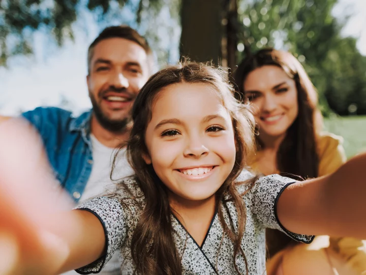 Une fille souriante prend un selfie avec ses parents.