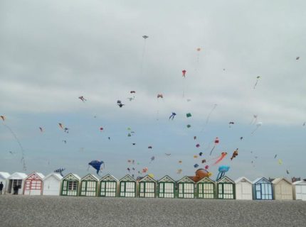 Des cerfs-volants colorés volent au-dessus des cabanes de plage.