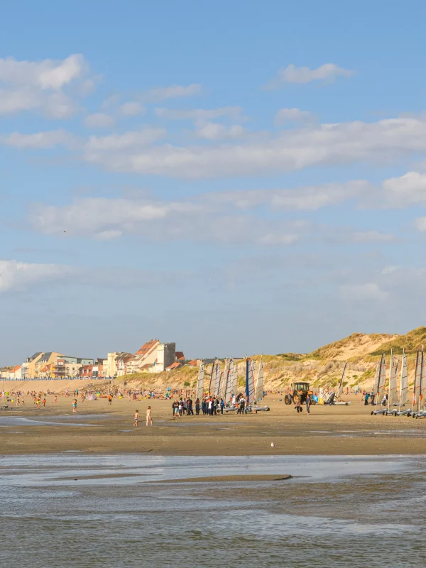 Plage animée avec voiliers et ciel dégagé.
