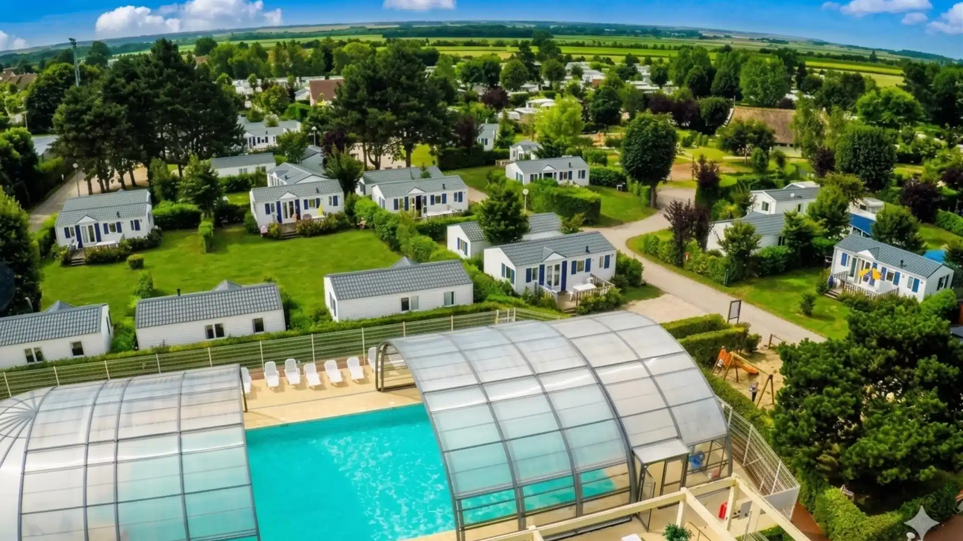 Vue aérienne d'un camping avec piscine et cottages.